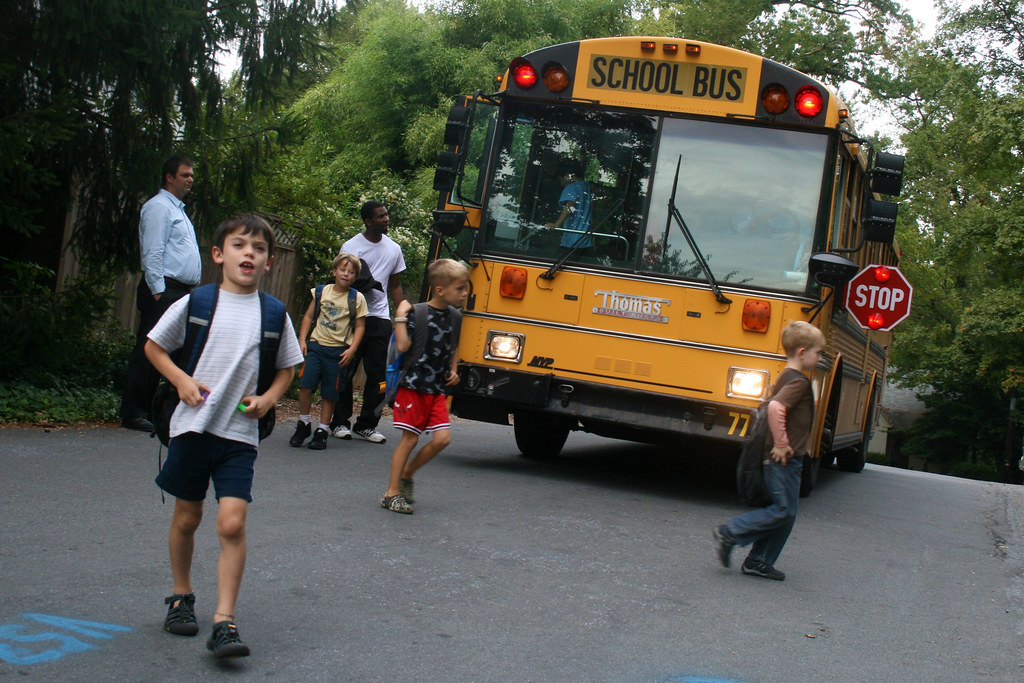 School bus with its stop sign our and letting kids cross in front of it.