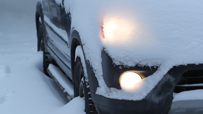 Snow fall covered the headlights of a vehicle during winter diriving.